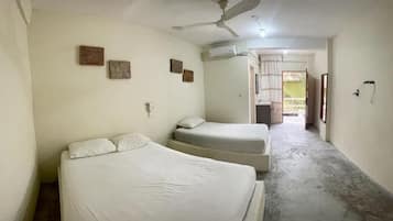 Una habitación con dos camas, un ventilador de techo y una puerta que da a un balcón.