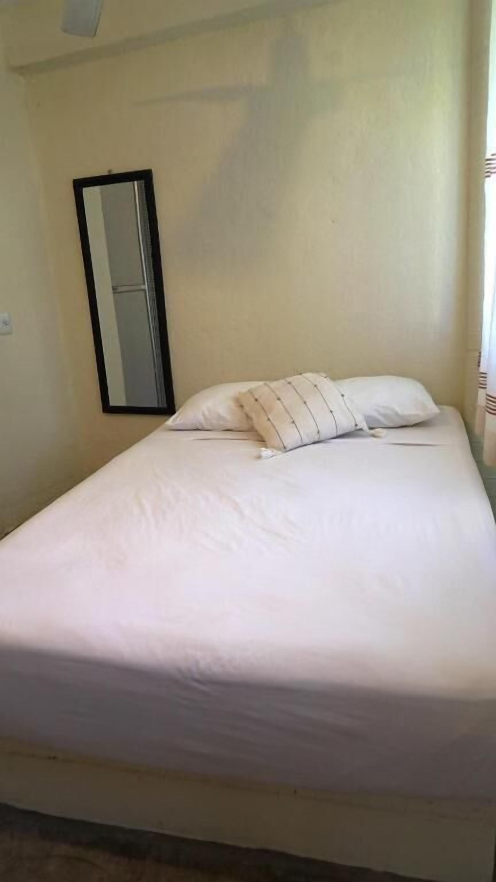 Una cama individual con ropa blanca y dos almohadas, un espejo montado en la pared y una pared lisa.