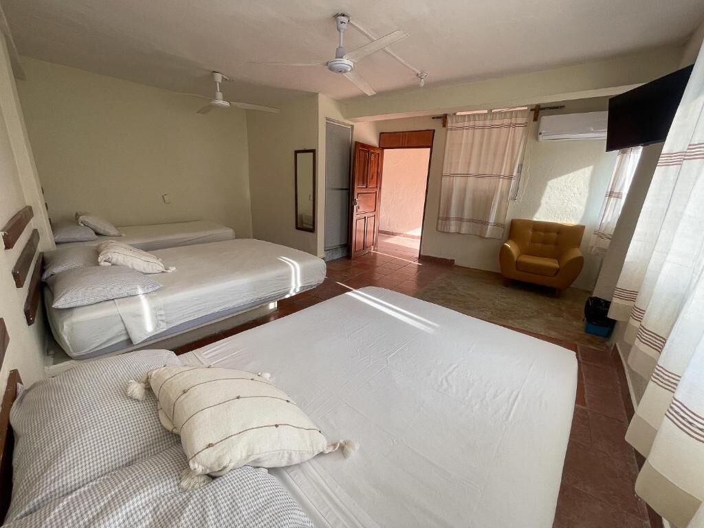 Habitación de hotel con tres camas, ventilador de techo, televisión y una silla.