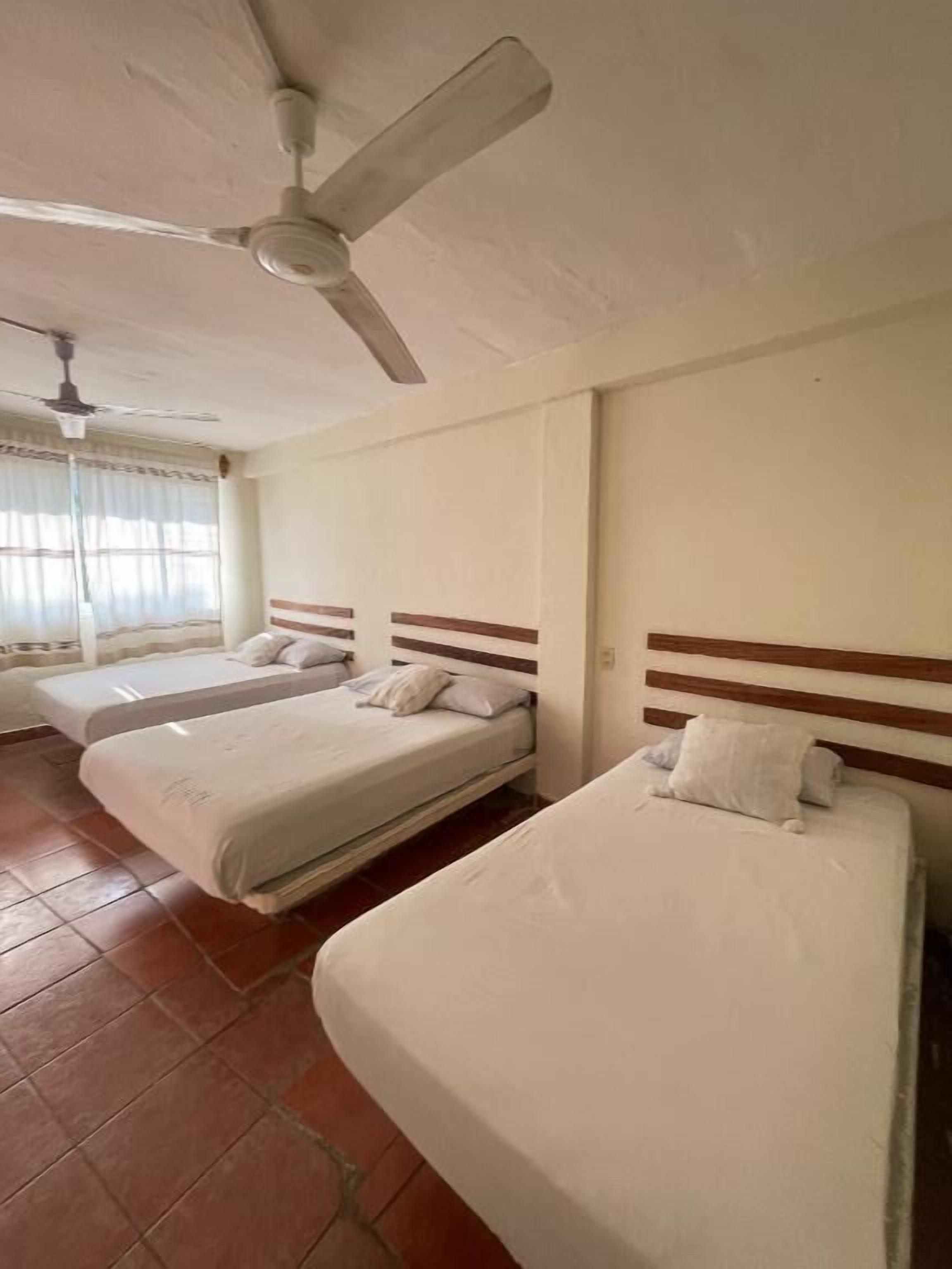 A hotel room with three beds, a ceiling fan, and a window with curtains.