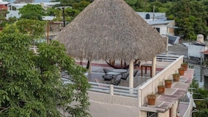 A thatched-roof structure with outdoor seating, overlooking a coastal area with buildings and greenery. - Casa Laani (San Pedro Mixtepec)