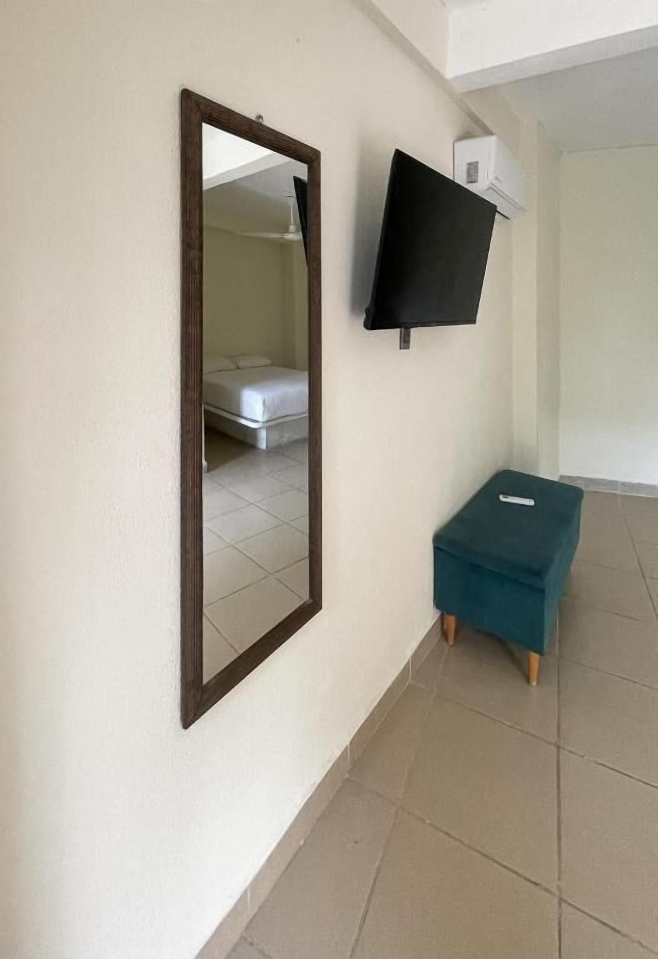 Una habitación con un espejo grande, un televisor de pantalla plana montado en la pared y un pequeño taburete turquesa.