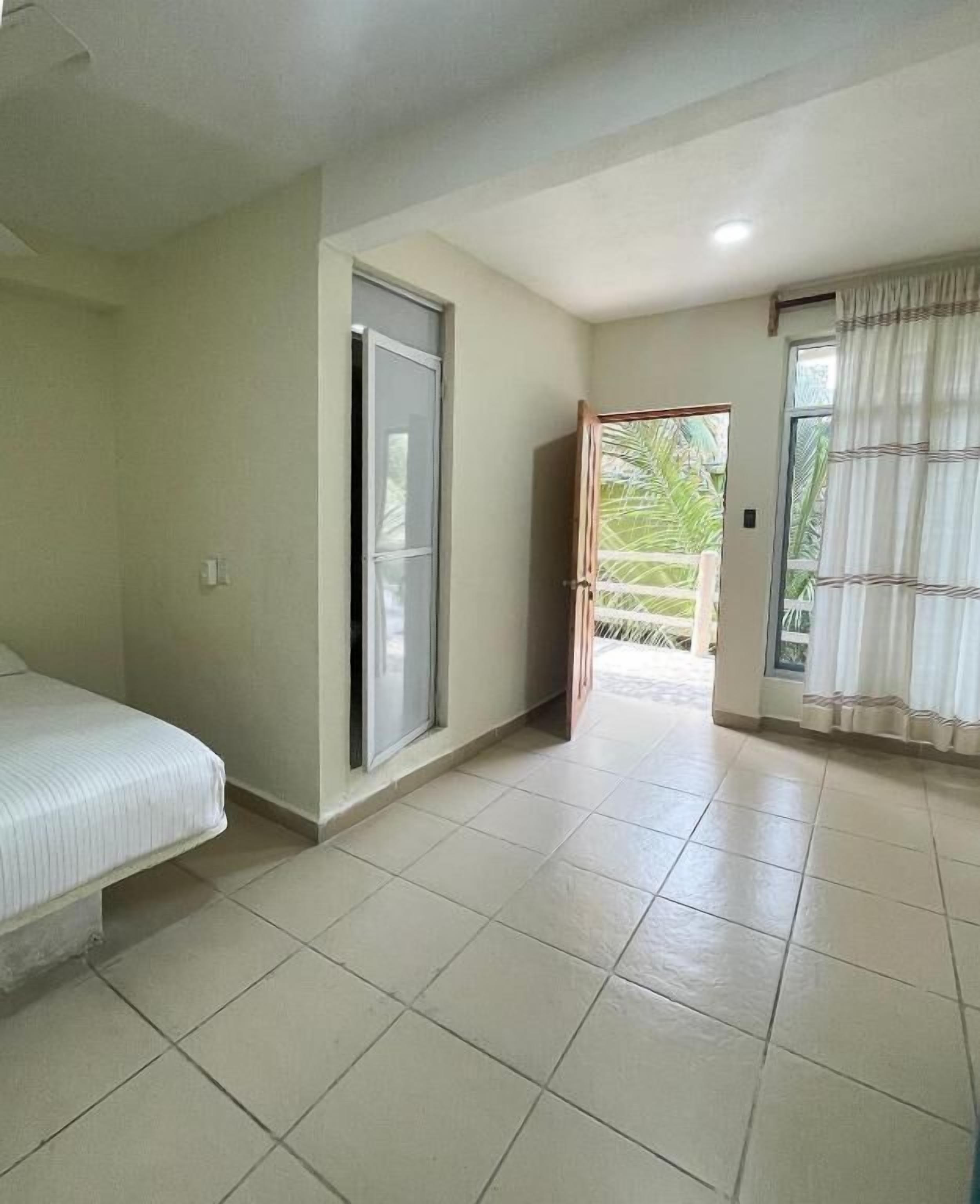 Una habitación con cama, una puerta corredera que da a un balcón y una ventana con cortinas.
