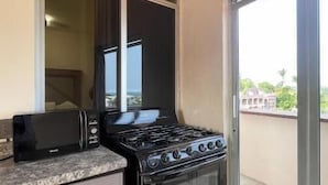 A compact kitchen with a stove, microwave, and a sliding glass door leading to a balcony. - Casa Laani (San Pedro Mixtepec)