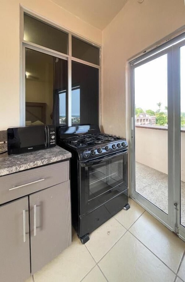 A compact kitchen with a stove, microwave, and a sliding glass door leading to a balcony. - Casa Laani (San Pedro Mixtepec)