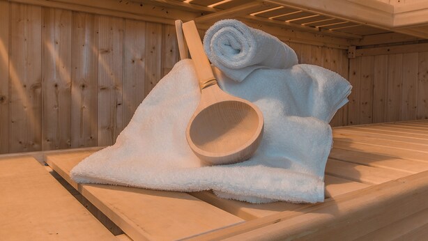 A wooden sauna with a bench, a rolled-up towel, and a wooden ladle. - Naturparkhotel & Landgasthof Stromberg (Sachsenheim)