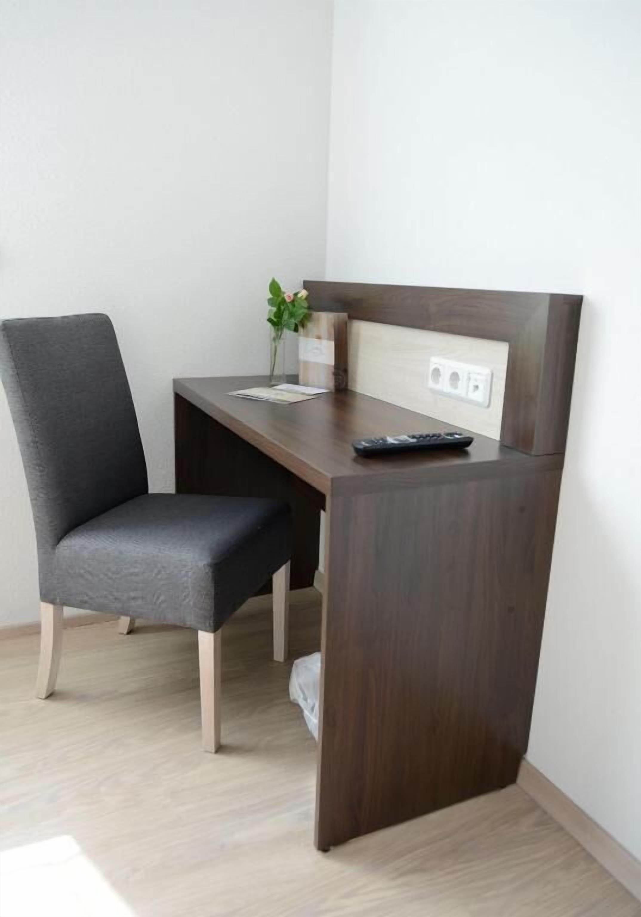 A small, dark wood desk with a chair, a remote control, and a small potted plant.