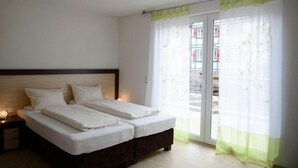 A bedroom with two beds, a nightstand, and a window with sheer curtains. - Naturparkhotel & Landgasthof Stromberg (Sachsenheim)