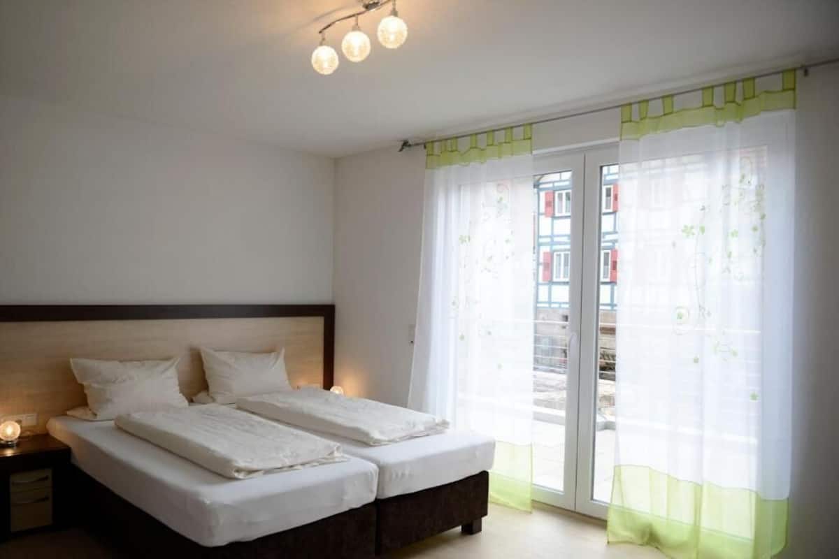 Ein Schlafzimmer mit zwei Betten, einem Nachttisch und einem Fenster mit durchsichtigen Vorhängen.