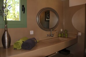 Une salle de bain équipée d’un lavabo, d’un miroir, d’un vase avec des fleurs, de serviettes et d’articles de toilette.