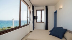 A bedroom with a large window, a bed with blue pillows, a flat-screen TV, and a door with a blue frame. - Guest House B&B Villa Ziella (Pachino)