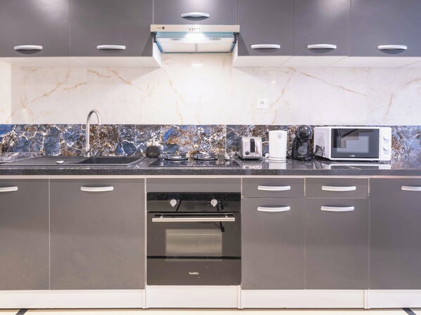 A modern kitchen with grey cabinets, a black countertop, a built-in oven, a microwave, and a coffee maker.