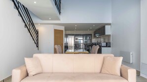 A modern living room with a beige sofa, a staircase, and a kitchen in the background.