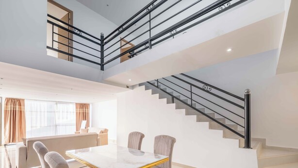 A spacious living area with a high ceiling, a staircase with black railings, and a dining table with chairs.