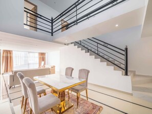 A spacious living area with a high ceiling, a staircase with black railings, and a dining table with chairs.