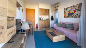 Un salon moderne avec un meuble en bois, un tapis bleu, une table basse en bois, un canapé rose et un tableau abstrait coloré accroché au mur.