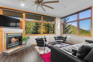 Un moderno salón con chimenea, muebles de cuero y grandes ventanales con vistas al bosque.