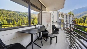 Ein Balkon mit Tisch und Stühlen mit Blick auf ein bewaldetes Tal und einen Berg.