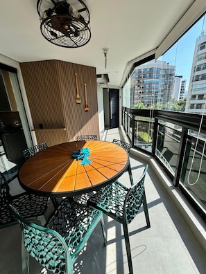 A round wooden table with chairs, a ceiling fan, and a view of tall buildings. - Beachfront Apartment Set Back from the Setback (Bertioga)