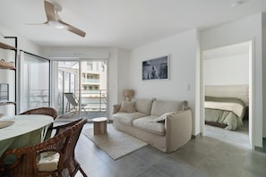 A modern living room with a sofa, dining table, wicker chairs, a ceiling fan, and a view through a glass door to an outdoor balcony. - Chic Apartment with Private Terrace and Wi-Fi in Pornic (Pornic)