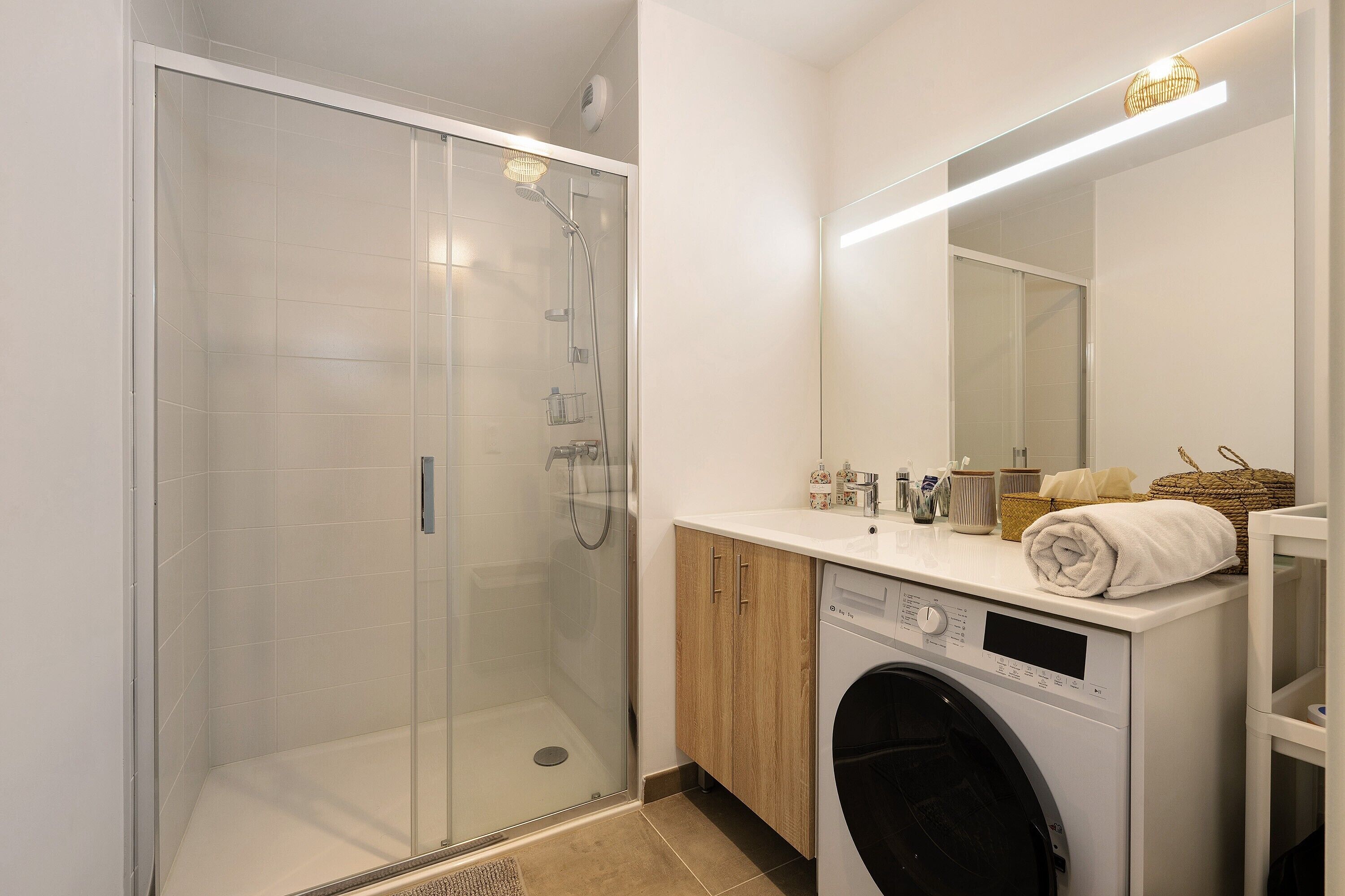 Un baño moderno con ducha de vidrio, lavadora y espejo sobre el lavamanos.