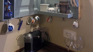 Una cocina con una estantería que tiene tazas y una cafetera.