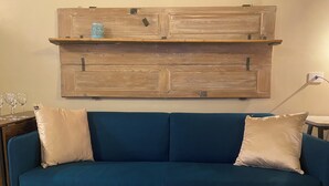 Un sofá azul con dos almohadones, un estante de madera arriba y una mesita de noche con una lámpara.
