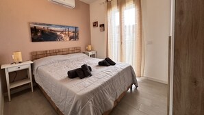 A bedroom with a large bed, a bedside table with a lamp, a painting on the wall, and a window with curtains. - Sea View Residence with Pool (Lu Bagnu)