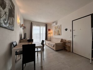 A modern living room with a dining area, a sofa, a TV, and artwork on the walls. - Sea View Residence with Pool (Lu Bagnu)