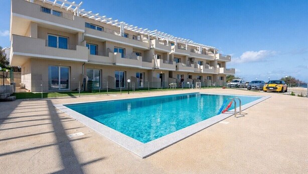 A multi-story hotel with a swimming pool, balconies, and a clear blue sky. - Sea View Residence with Pool (Lu Bagnu)