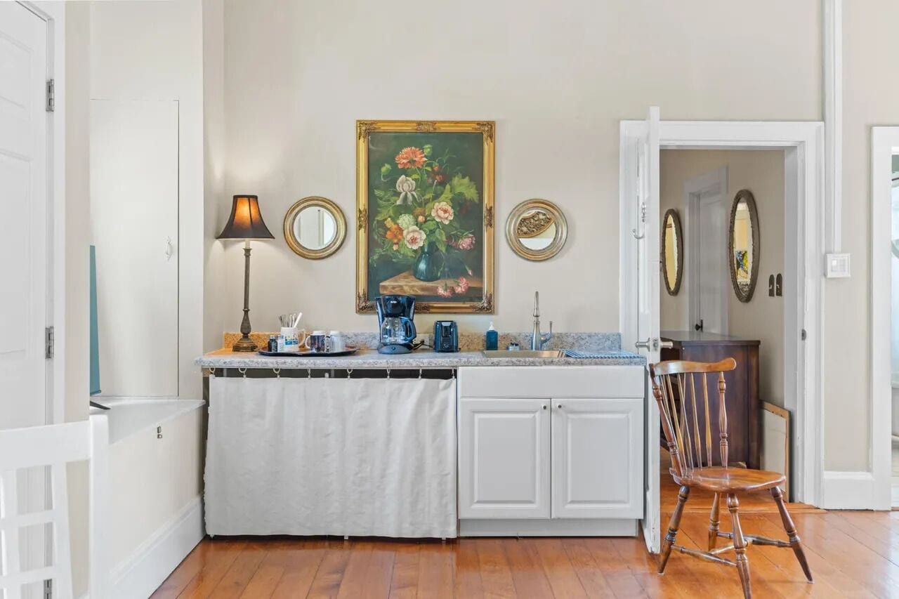 Una cocina con encimera blanca, cafetera, lámpara y un cuadro de flores en la pared.