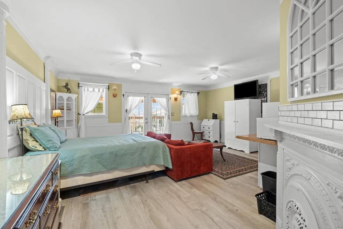 Un dormitorio con cama, una silla roja, cómoda, televisor y chimenea.