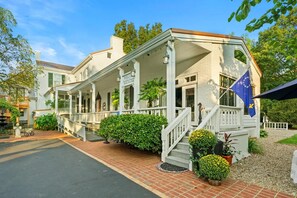 A historic building with a covered porch, a flag, and a welcoming sign.