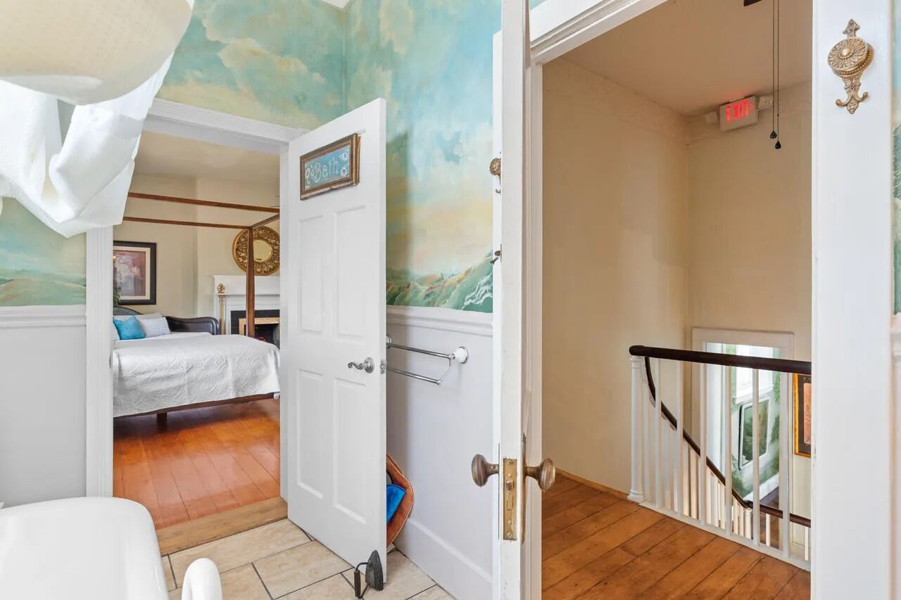 A bedroom with a bed, a door leading to another room, and a staircase with a railing.