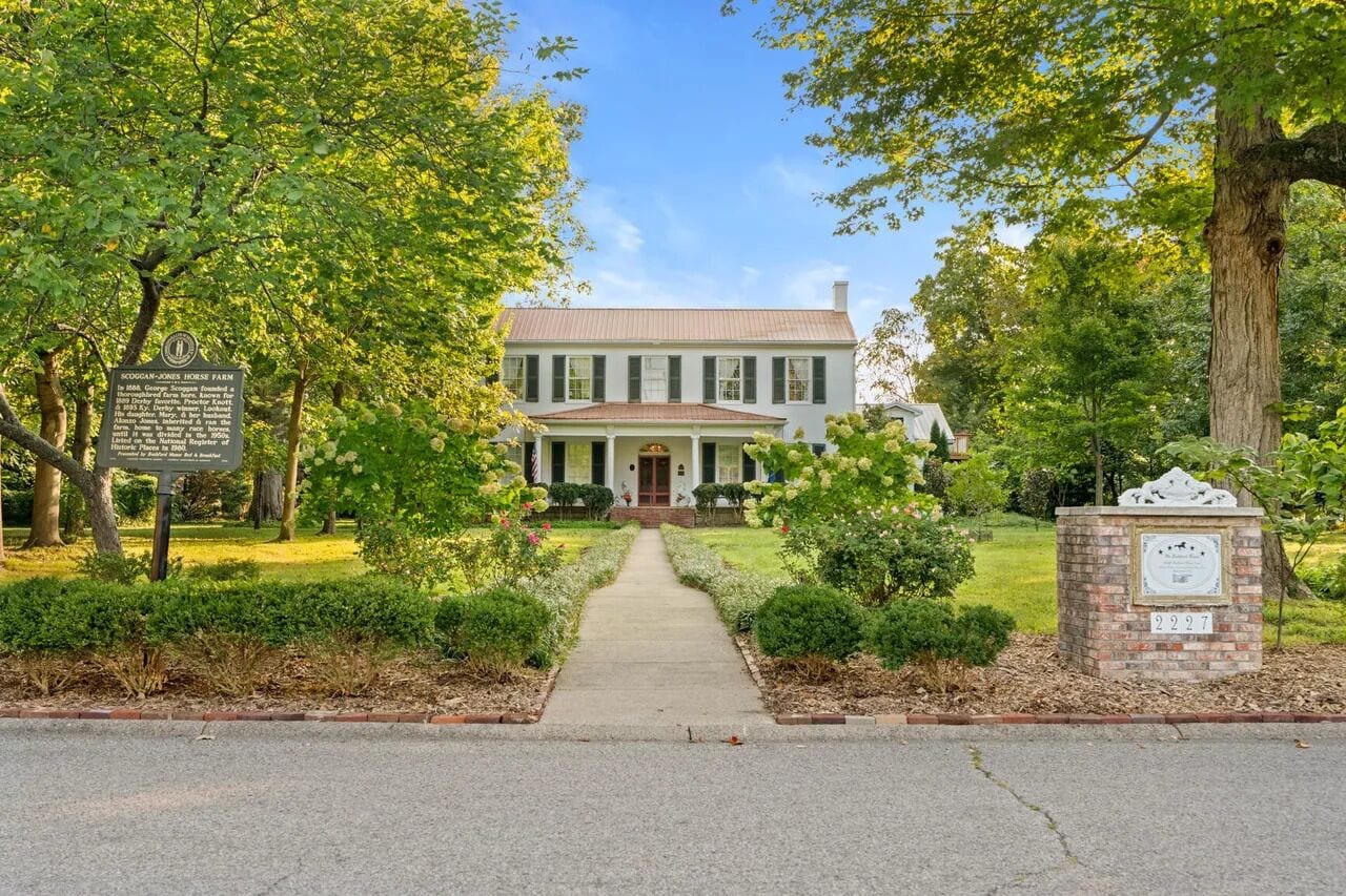 A historic house with a central entrance, surrounded by well-maintained gardens and trees.
