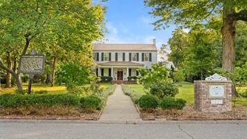 A historic house with a central entrance, surrounded by well-maintained gardens and trees.