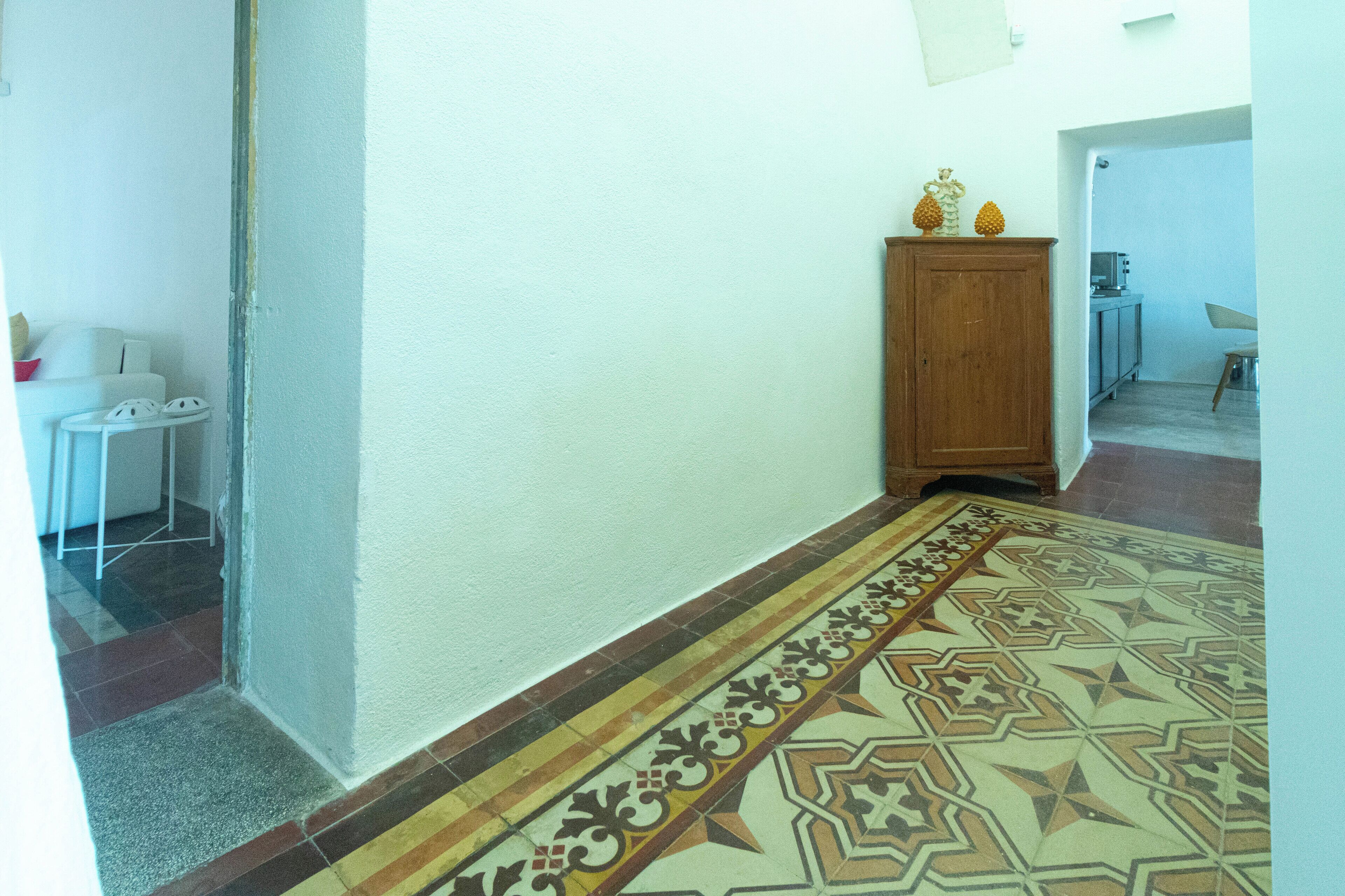 A hallway with patterned flooring, a wooden cabinet, and a small table with a chair.
