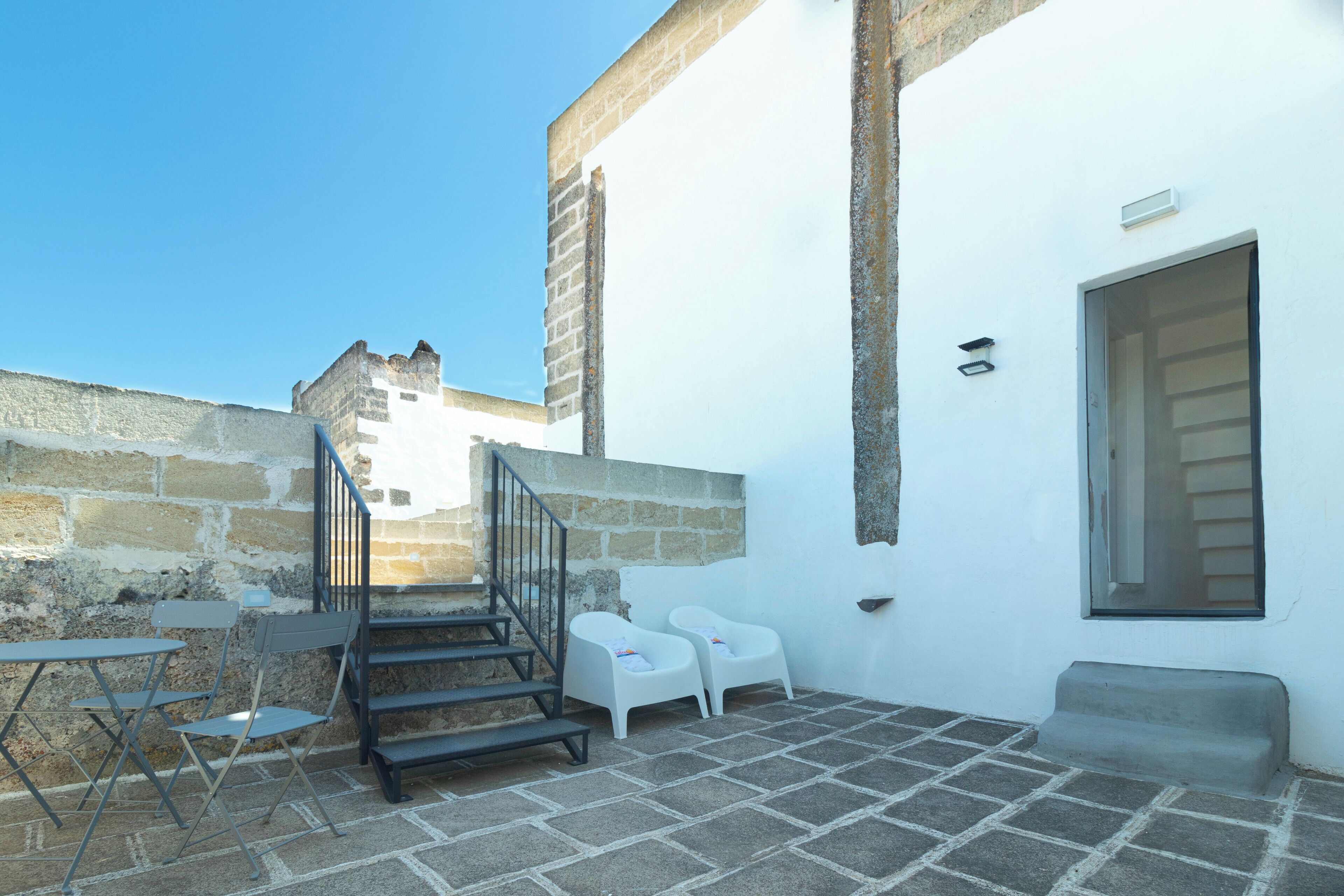 A courtyard with stone flooring, a set of stairs, white chairs, and a small table.
