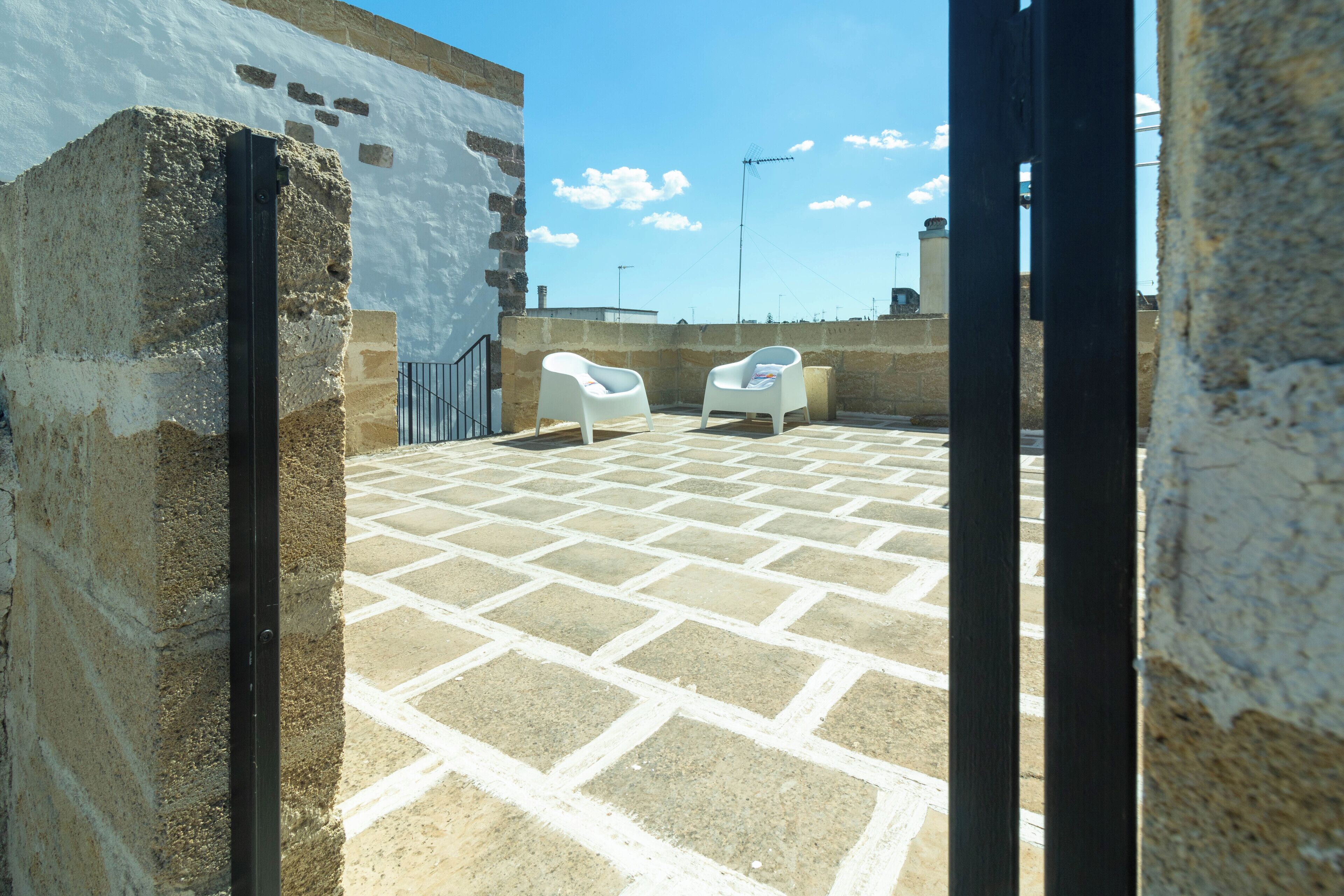 Une terrasse sur le toit, avec un sol carrelé, deux chaises blanches et un mur en pierre.