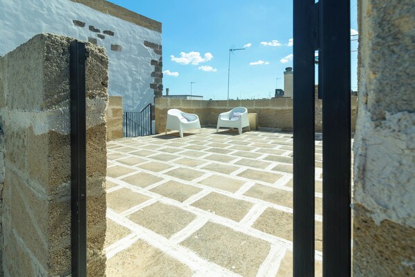 A rooftop patio with a tiled floor, two white chairs, and a stone wall. - Dimora Zenieri Terrazze e Piscina (Casarano)