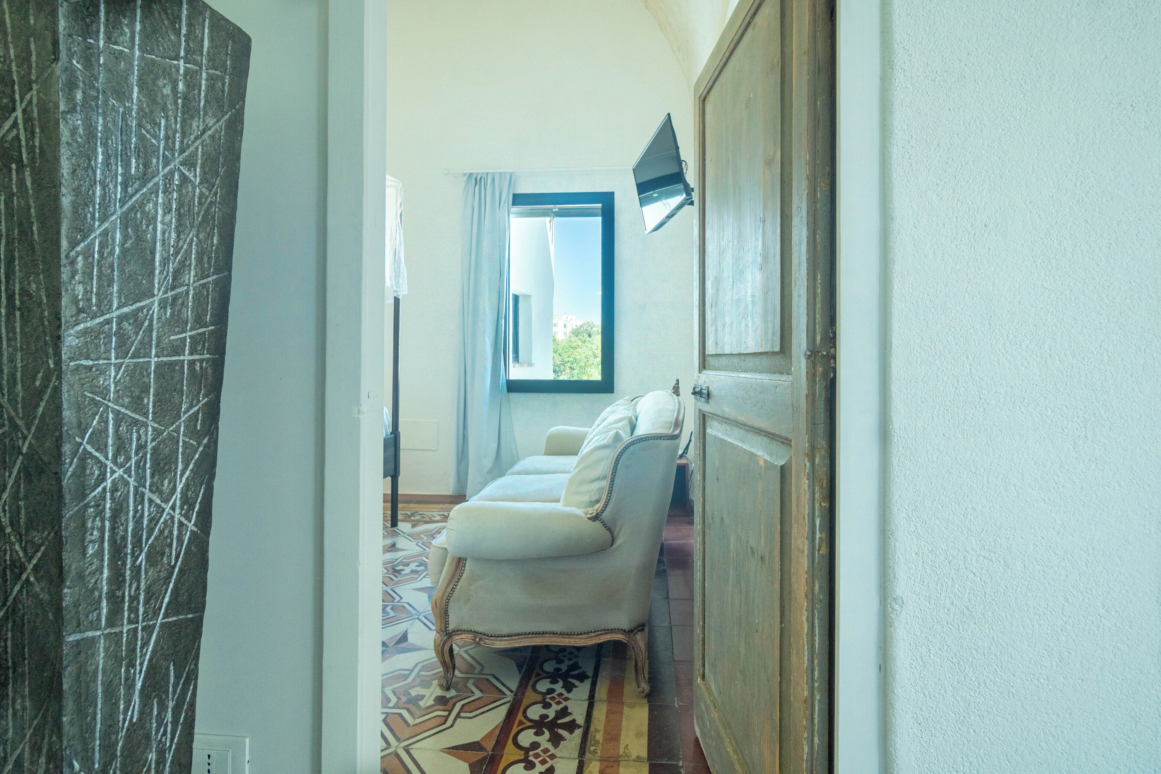 A hallway with a patterned floor, a white sofa, and a window with curtains.