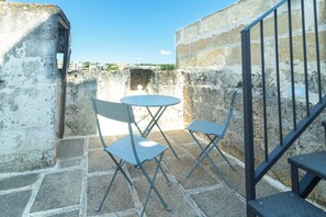 Eine Terrasse mit Tisch und zwei Stühlen, eine Steinsäule und ein Blick auf Gebäude in der Ferne.