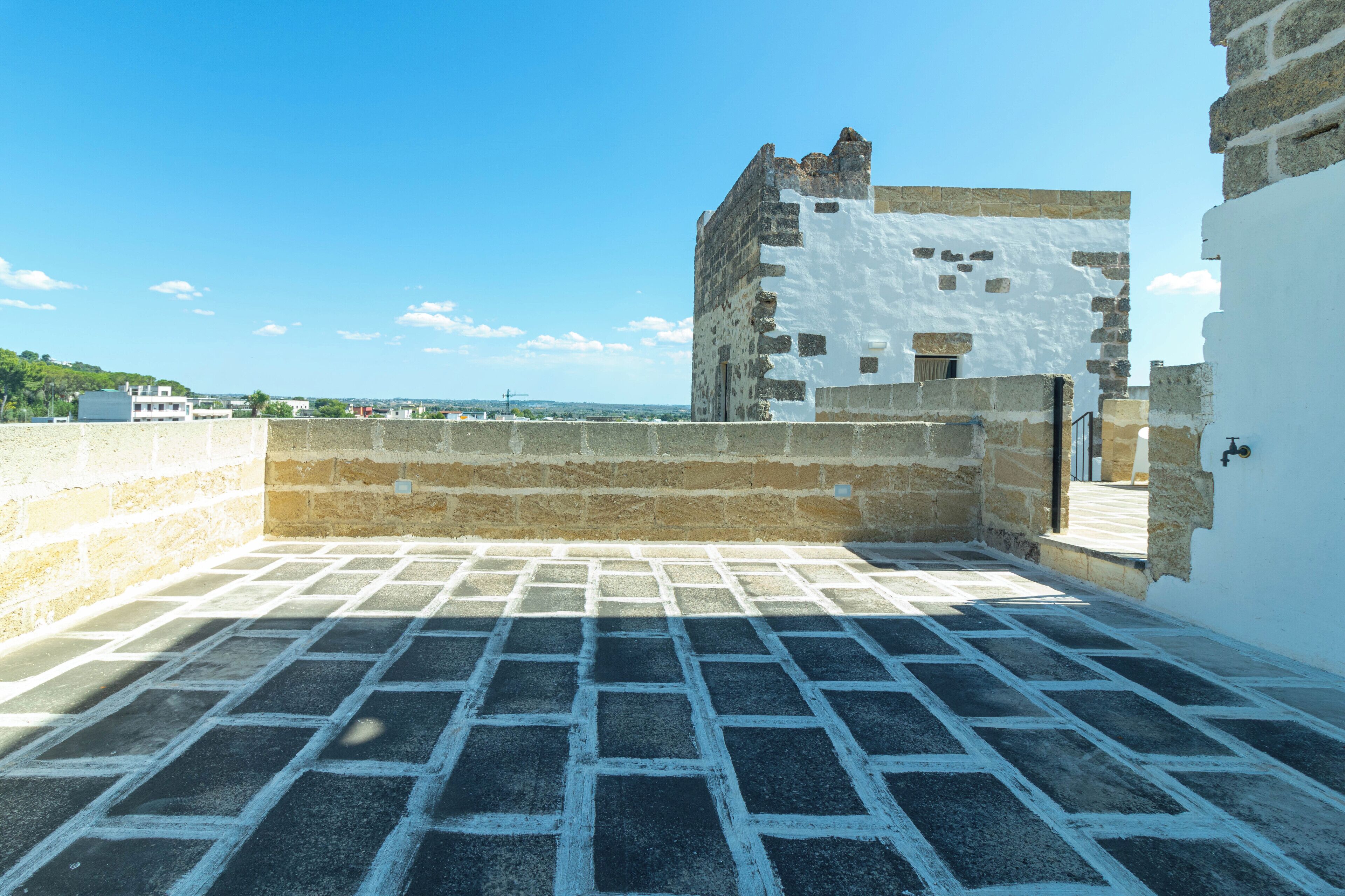 Eine Dachterrasse mit einem gemusterten Boden, einer Steinwand und Blick auf ein historisches Gebäude.