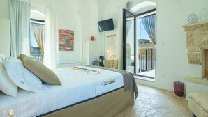 Habitación de hotel con cama, televisión fijada a la pared, balcón con vistas y chimenea de piedra.