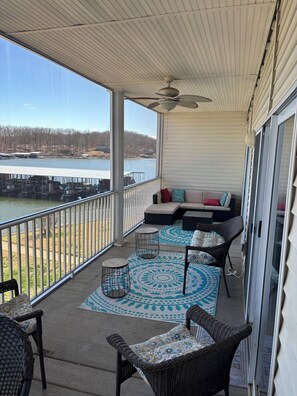 A covered balcony with a view of a lake, a seating area with cushions, and a patterned rug. - Spacious waterfront 3-bedroom condo in pleasant Sunrise Beach with pool access (Sunrise Beach)