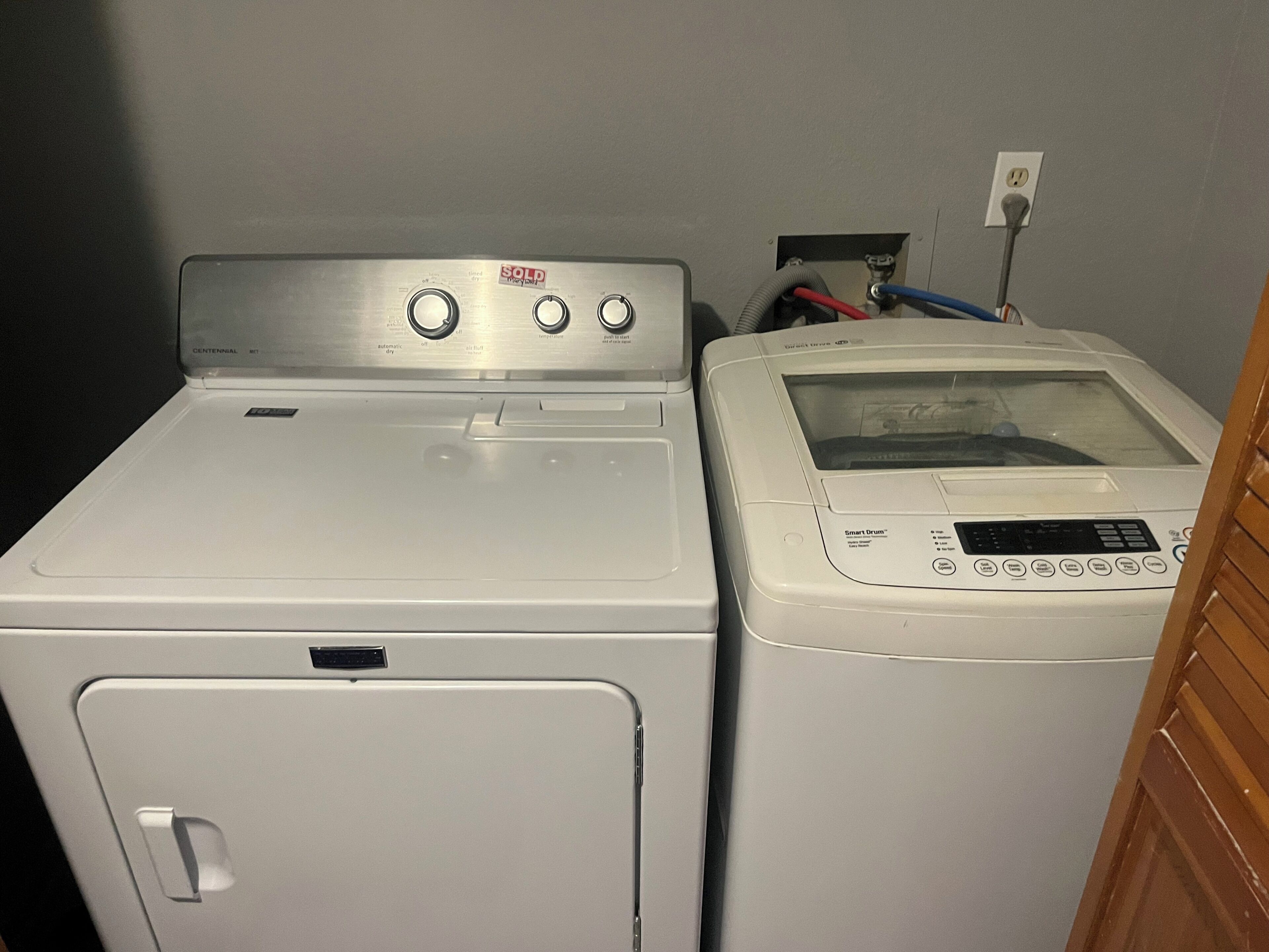 Lavadora y secadora de carga frontal en un cuarto de lavado, con un enchufe y un panel de control a la vista.