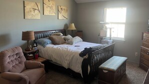 A bedroom with a bed, a chair, a nightstand, a lamp, a window, and artwork on the wall. - Adorable townhome with in Blue Springs 10 Miles from GEHA STADIUM (Blue Springs)