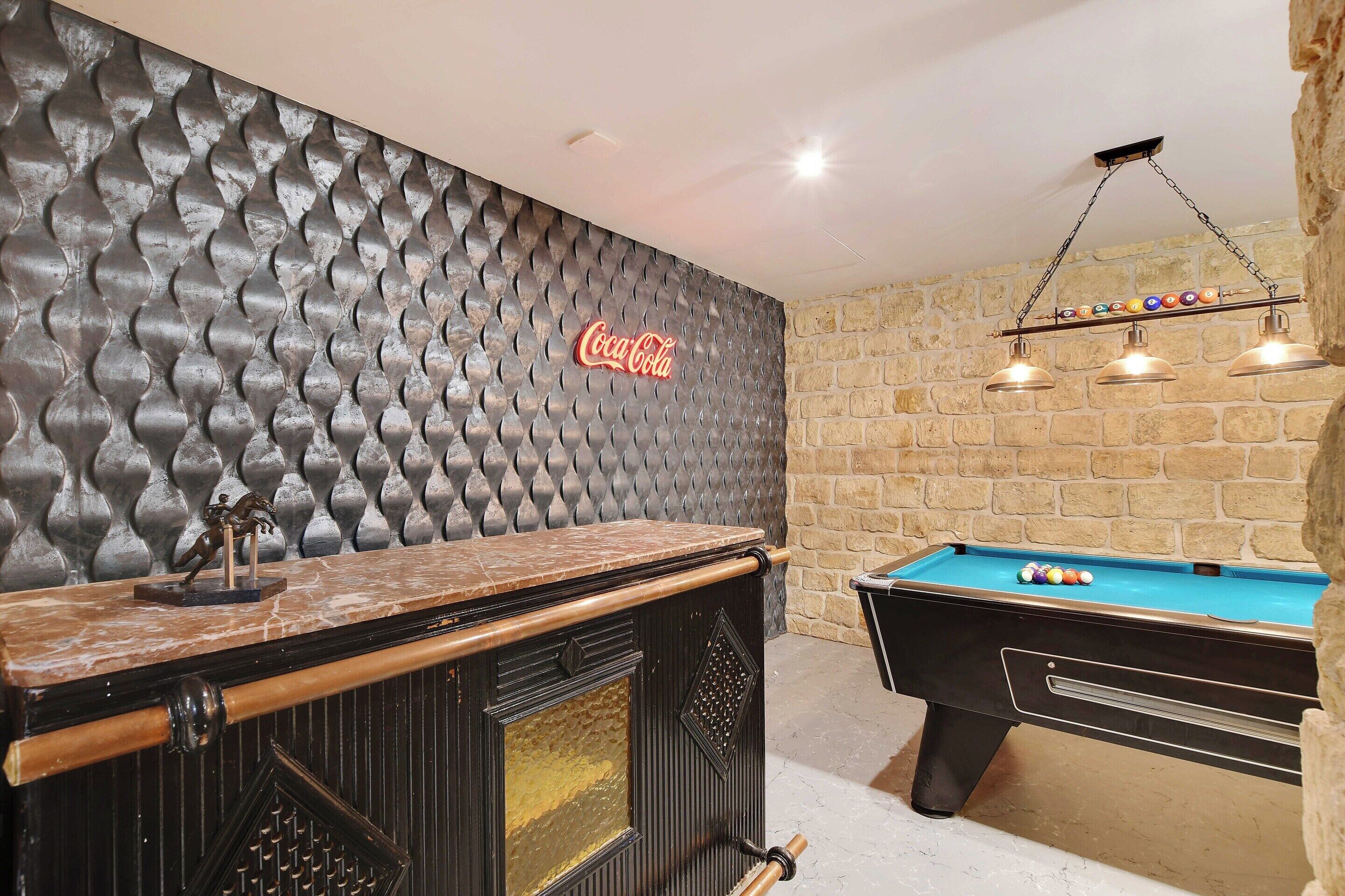 Une table de billard, une table de jeu de pool et un coin bar agrémenté d’une enseigne Coca-Cola.