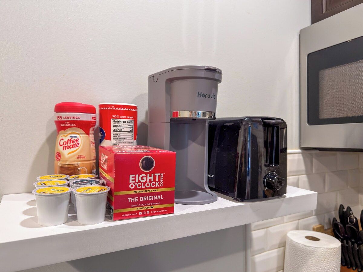 A kitchen counter with a coffee maker, a box of coffee pods, a container of coffee creamer, and a roll of paper towels.