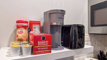 A kitchen counter with a coffee maker, a box of coffee pods, a container of coffee creamer, and a roll of paper towels.